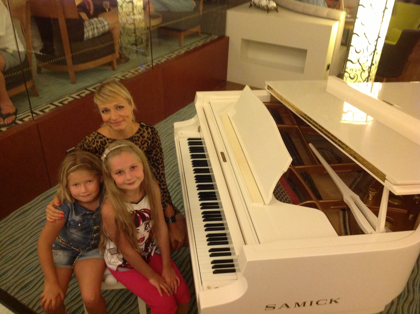 Tetiana giving a piano lesson to two young students at the keyboard.